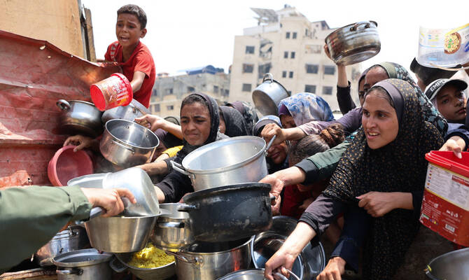 Palestinians gather to receive cooked meals from a food distribution center in Gaza City on August 13, 2025. (AFP)