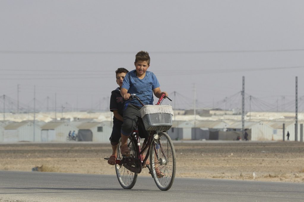 Young Syrian refugees ride a bicycle at the Azraq camp for Syrian refugees in northern Jordan on August 2, 2018. (AFP)