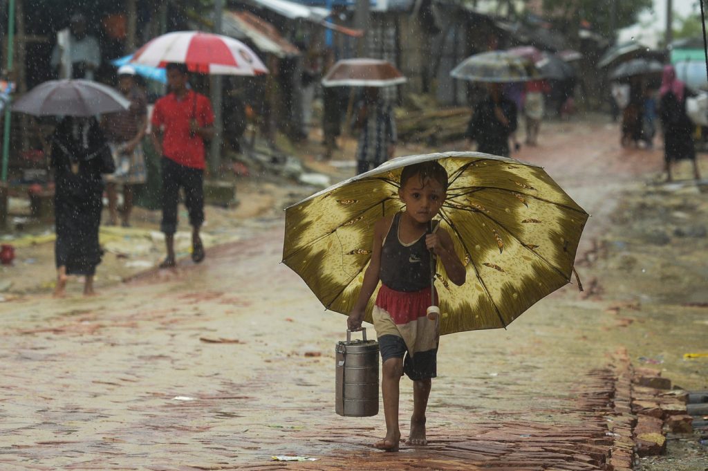 モンスーンの大雨の中、傘の下で雨を避けるロヒンギャ難民の少年。2019年9月12日、ウヒアのクトゥパロン難民キャンプにて。（AFP）