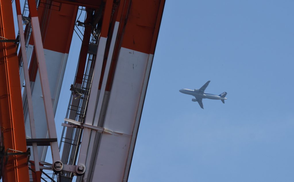 2016年2月18日、東京の埠頭のコンテナヤードのクレーン車の上を飛ぶ飛行機。（AFP）