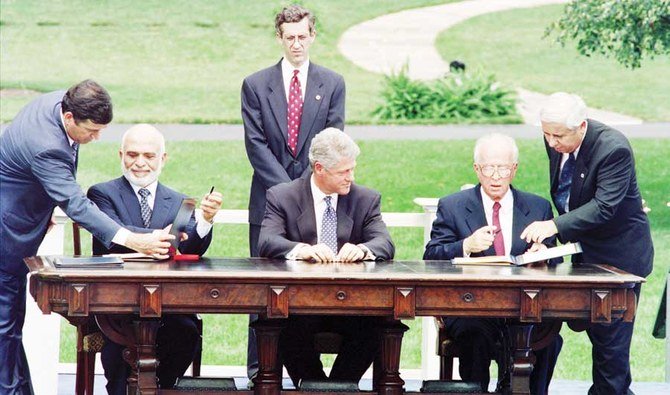 1994年7月25日にワシントンのホワイトハウスで式典が行われる中、イスラエルのイツハク・ラビン首相（右から2番目）とヨルダンのフセイン国王（左から2番目）が米国のビルクリントン大統領（中央）が見守る中、身元不明の補佐官により署名する場所を指示される様子（AFP）　