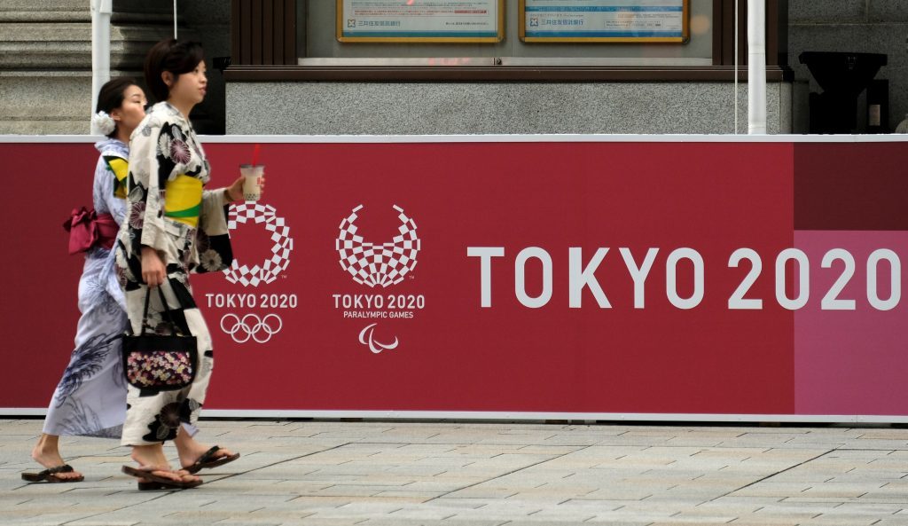 2019年7月23日に開催される東京2020オリンピックのロゴを展示するボードの前を歩く人々。(AFP)