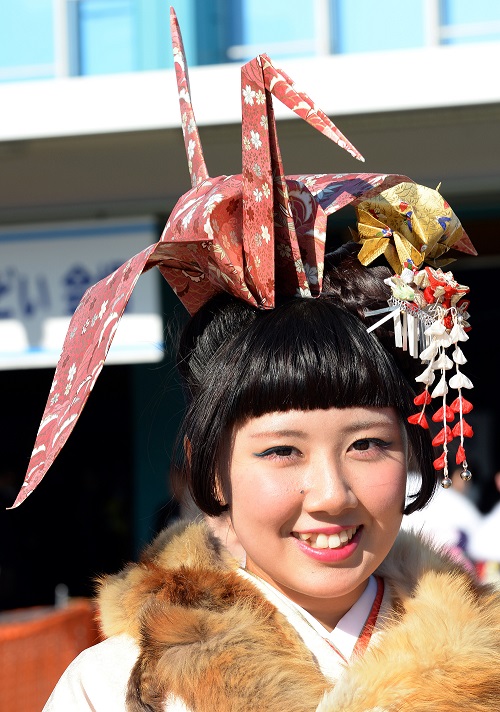 東京の豊島園遊園地で2014年1月13日に開催された「成人の日」祝賀式典に参加し、大きな「折り鶴」の飾りを乗せて微笑む20歳のヤマグチマホさん。(資料写真/AFP)