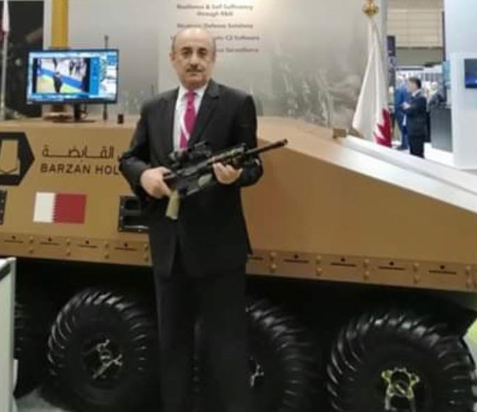 東京で開催されたDESIで、カタール製のビンディグARXライフルを持ち、モデルの前でポーズを取るハッサン・アル・エマーディ駐日カタール大使。(提供写真)
