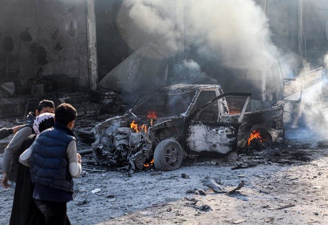 北部シリアの街、タル・アブヤドの工場地帯で、自動車爆弾の爆発後に燃え上がる車の横を支えられながら歩く女性。(ファイル/AFP)
