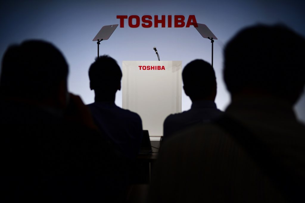 東京で開催される記者会見をひかえ、東芝のロゴの前に座るジャーナリストたち。2018年11月8日。（AFP）