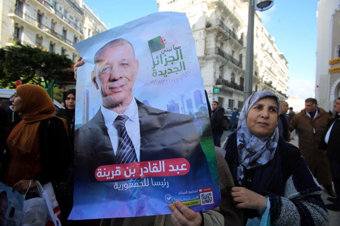 2019年11月17日アルジェリア・アルジェにて、大統領選候補者アブドゥルカーディル・ベングリーナの選挙戦開始とともにポスターの隣でポーズをとる支持者。（ロイター）