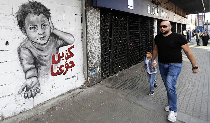 北部の港湾都市タラーブルスのアル=ヌール広場の建物の壁に描かれた落書きの前を通り過ぎる男性。（AFP）