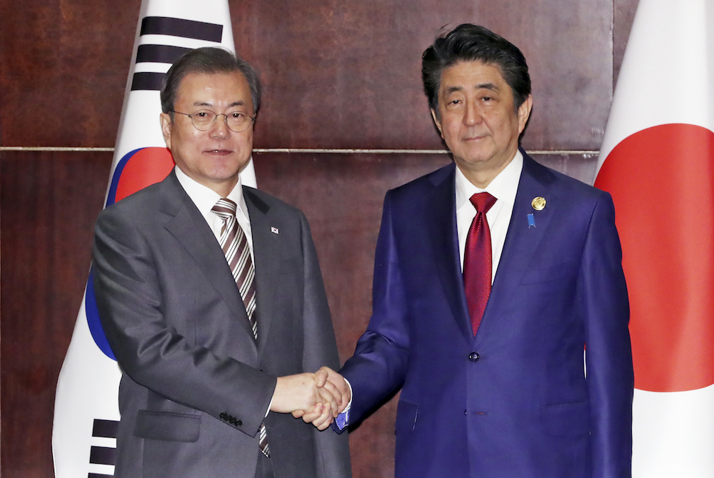 韓国の文在寅大統領（左）が、日本の安倍首相と握手している。（AFP） 