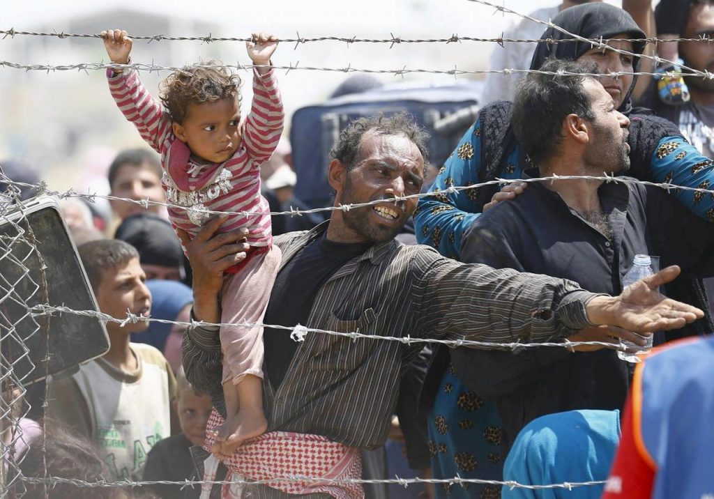トルコ・シャンルウルファ県アクチャカレ郡の国境ゲートでトルコ入境を待つシリア人難民が娘を抱き寄せている。（ロイター）