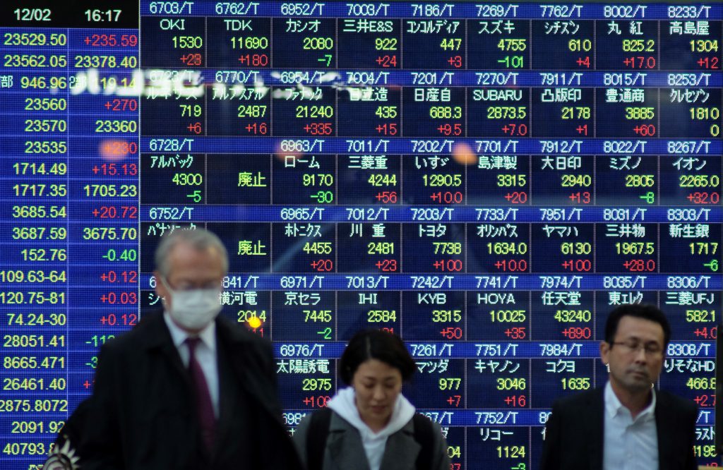  2019年12月2日、東京の東京証券取引所に上場する日経225の株価を表示した電光相場表示板の前を通り過ぎる歩行者たち。