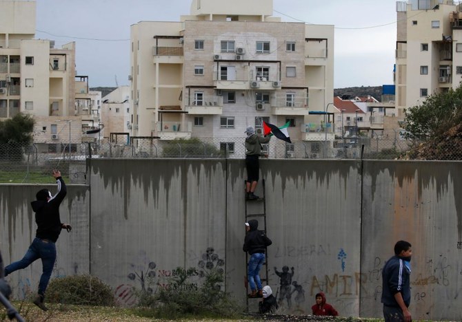 イスラエルがさらに多くの領土併合を計画する占領下のヨルダン川西岸で、論争の的となっている防御壁をよじ登るパレスチナの抗議者たち。(AFP)