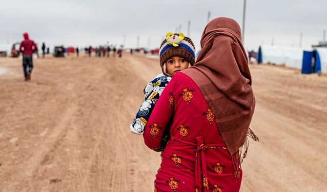 2020年2月17日、シリア北東部のクルド人が多数を占める都市ハサケの近郊、国内避難民のためのワシュカンニ・キャンプ内を子どもを抱いて歩くシリアの女性。（AFP）