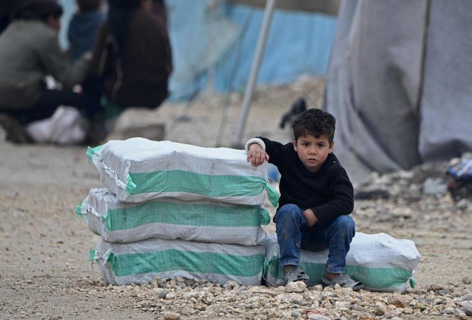 2020年2月21日、トルコとの国境沿いにあるデイル・アル・バルートの町の近くにあるメフメディエの町の難民キャンプで、燃料と飲料水からなる救援物資の横に座る避難民のシリアの少年。（AFP）