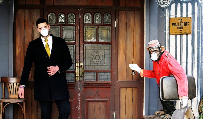 イスラエル占領地のヨルダン川西岸にあるベツレヘムのザ・ウォールド・オフ・ホテルの入り口で、コロナウイルスの予防策としてマスクを着用するホテルの従業員とチンパンジーのベルボーイ像。（ロイター）