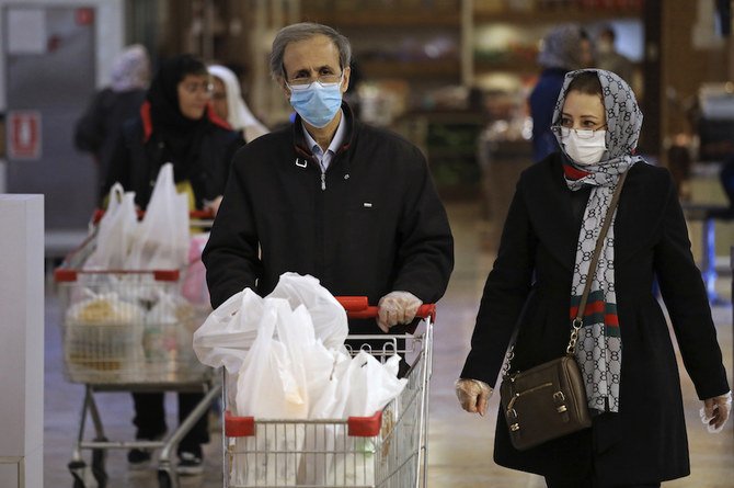 イランのテヘラン北部で、マスクと手袋をつけて買い物をする人々。同国の政府はコロナウイルスの流行を隠蔽したと非難されている。（AP通信）