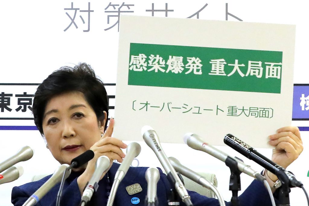 2020年3月25日、東京でCOVID-19コロナウイルスの感染拡大に関する記者会見の中で、日本語で「感染爆発重大局面」と書かれたボードを掲げる小池百合子東京都知事。（AFP通信）