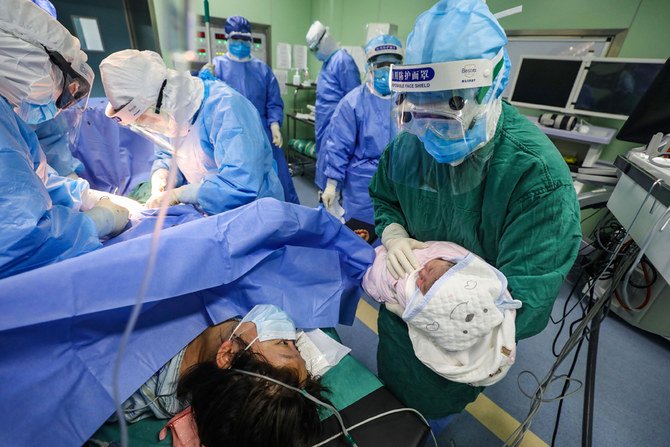 中国中央部の湖北省武漢の協和医院で2020年3月7日、新型コロナウイルスに感染した妊婦のために用意された婦人科・産科隔離病棟で帝王切開後に生まれた新生児をウイルス感染者の母親に見せる医療スタッフ（R）。（AFP）