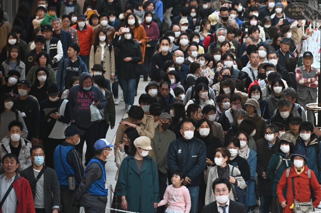 2020年3月21日、宮城県の仙台駅の外で展示された東京オリンピック2020の聖火を一目見ようとマスク姿で列に並ぶ人々（AFP）