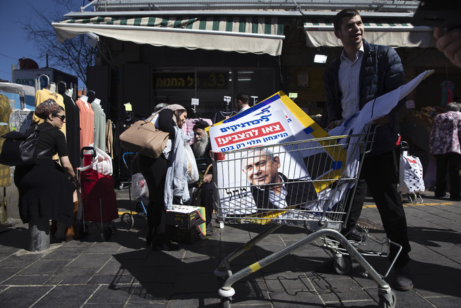 イスラエルのベンジャミン・ネタニヤフ首相の支持者の1人が、2020年2月28日にエルサレム内の市場でネタニヤフ氏の選挙運動集会が行われた後、スーパーマーケットのカートで選挙ポスターを運んでいる。（AP通信）