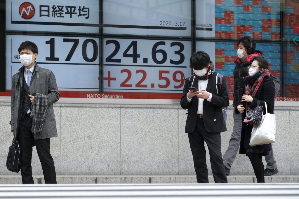 東京の東京証券取引所の株価を示す相場表示板の傍を通り過ぎる歩行者。(2020年3月17日、AFP)