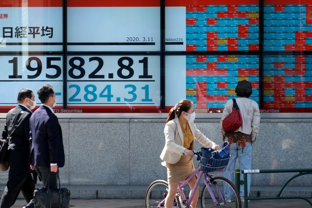 2020年3月11日、東京の東京証券取引所の株価を表示する相場表示板の前を通り過ぎる歩行者たち。