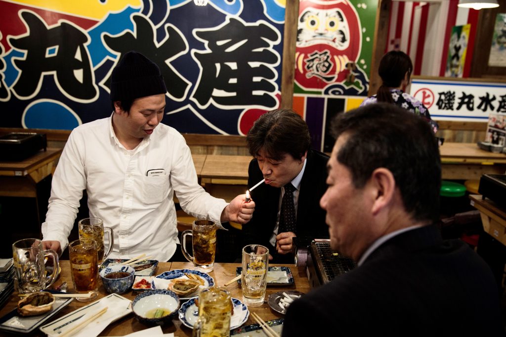 東京都有楽町近傍のレストランで昼食中に友人の煙草に火をつけている男性。2017年3月9日に撮られた写真。（AFP）