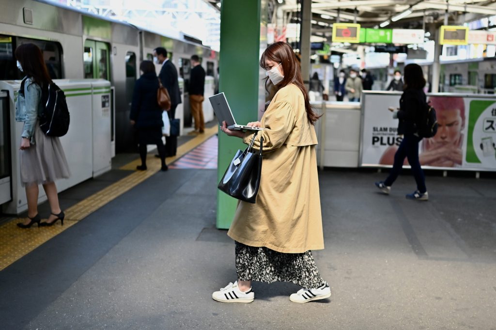 2020年4月8日、東京・五反田駅で電車に乗り込みながらノートパソコンで仕事をする女性。（AFP）