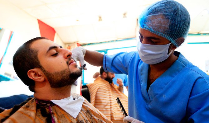 イエメンの首都サナアで2020年4月4日、COVID-19のコロナウイルスのパンデミックのさなか、マスクと手袋を着け利用客のひげをカットするイエメン人理髪師。（AFP通信）
