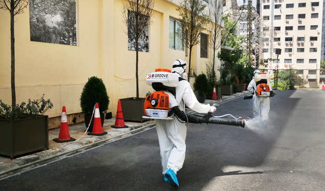 日曜日にベイルートで、国外から到着したレバノン人の乗客たちが感染検査を受けるホテルの外を、新型コロナウイルス予防措置として作業員たちが消毒剤をスプレーしている。（AP通信）