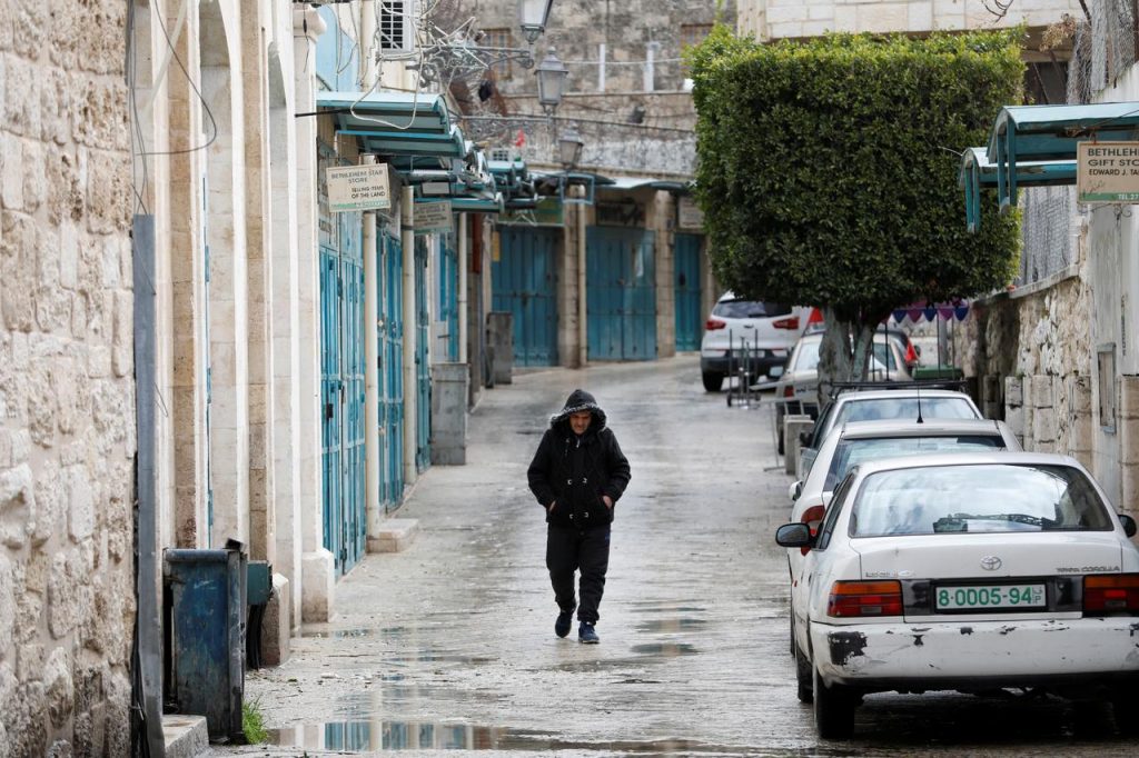 イスラエル占領下のヨルダン川西岸地区ベツレヘムで、新型コロナウイルス予防策として閉鎖された店の前を通り過ぎる人。（ロイター）