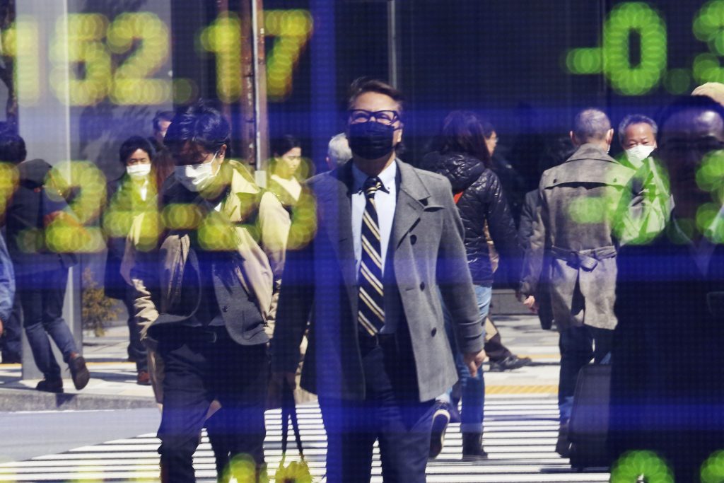 この2020年3月18日撮影の資料写真では、東京の証券会社の電子掲示板に人々が映し出されている。コロナウイルスの感染拡大により生産、輸出、設備投資が抑え込まれる中、日本の経済成長率は今年第1四半期にリセッションの状態にまで落ち込んだ。2020年5月18日に発表されたレポートによると、今後さらに景気が悪化するとの懸念は増大している。(AP)