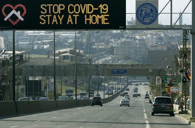 新型コロナウイルスの感染拡大を封じ込めるため人々に自宅にいるよう呼びかける道路標識の下を車が横断する。2020年4月14日、ベイルート東に位置するベイルート―ダマスカス国際高速道路において。（AFP）