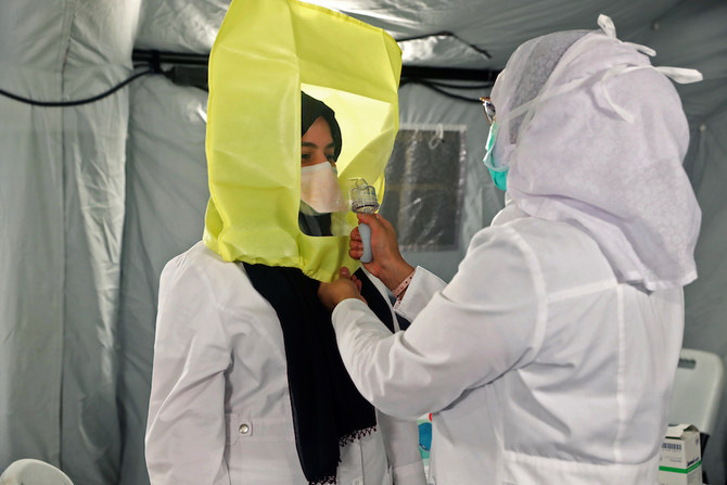 サウジアラビアのイスラム教聖地メッカにCOVID-19コロナウィルス患者を治療するために新規開設された野営病院のテントで、医療従業員が安全装具を着用するのを同僚が手伝う。（ファイル/AFP）