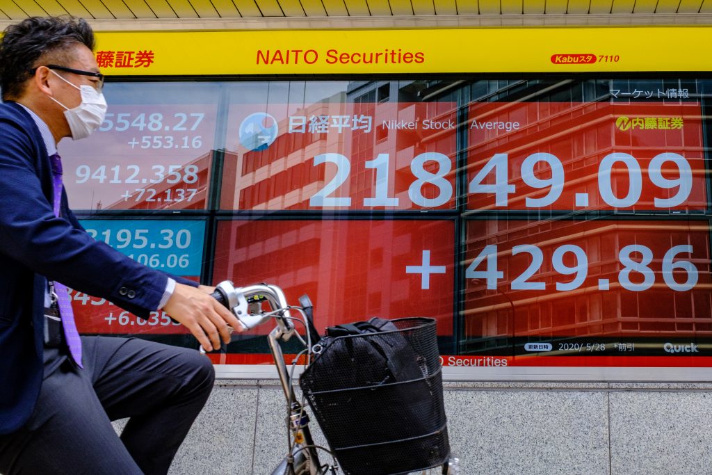 東京証券取引所の午前の日経平均株価を表示する電子株価ボードの前を通り過ぎるマスクを着けたサイクリスト、2020年5月28日、東京。(AFP)