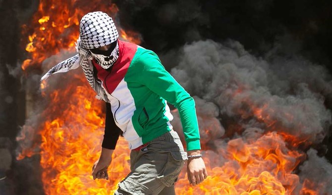占領下のヨルダン川西岸地区で金曜日に行われたデモで、イスラエル軍との衝突の中、燃えるタイヤの近くを歩く抗議者。(AFP)
