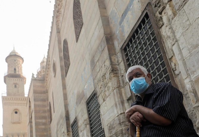 コロナウィルス感染症（COVID-19）を巡る懸念の中、ラマダンの聖なる月のイフタール（断食明けの食事）を前に、エジプトの古いカイロ・イスラム地区の閉鎖されたモスクとイスラム学校の正面で保護マスクを着用して座る男性。2020年4月30日。（ロイター）