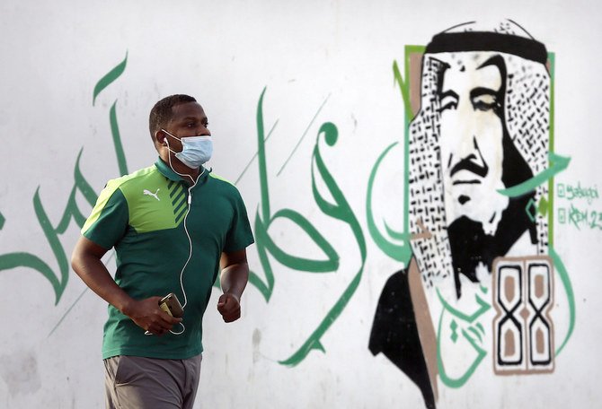 2020年6月28日日曜日、サウジアラビアのジェッダで落書きされたサルマン国王の肖像画の前を通り過ぎる男性は、コロナウイルスの蔓延を抑えるためにマスクを着用している。アラビア語は、「安全な祖国のために」と書いている。 (AP)