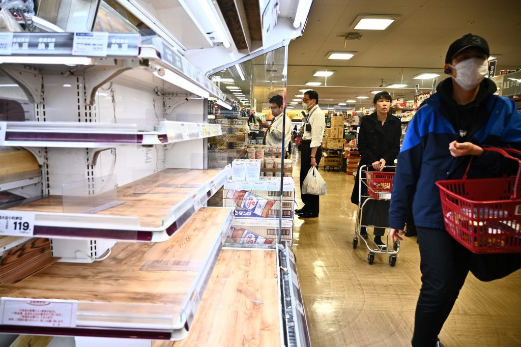 2020年4月6日、東京のスーパーマーケットの空っぽの食品棚のそばで人々が買い物をしている。（AFP）