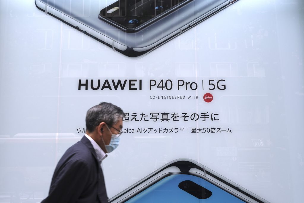 2020年6月27日に撮られたこの写真には、東京の中国の電気通信会社ファーウェイの最新スマートフォンの広告の前を、男性が通り過ぎる姿が写っている。（AFP通信）
