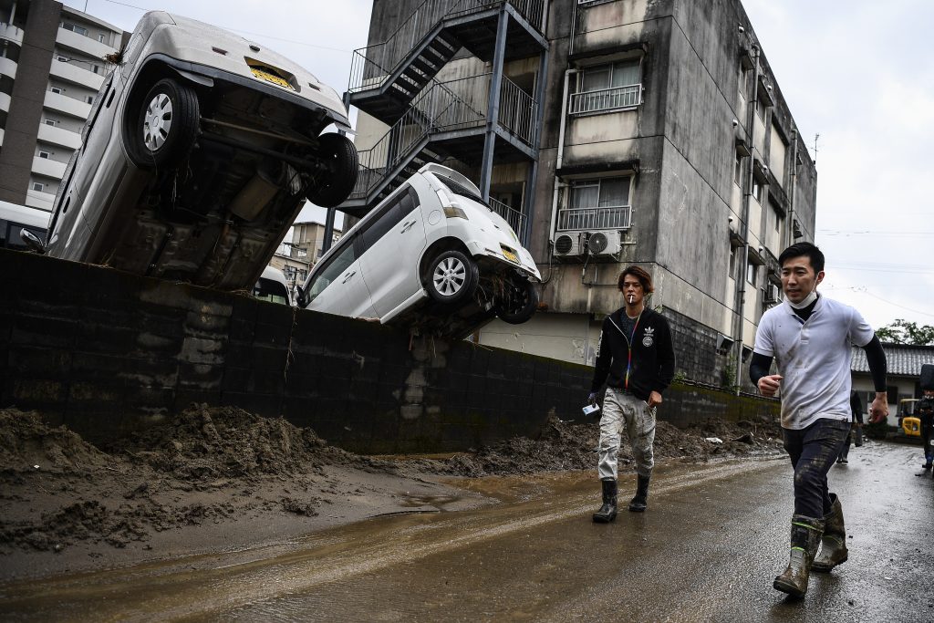 熊本県人吉市で最近の洪水により逆さまになった自動車の横を通り過ぎる男性たち。2020年7月10日。この地域は激しい雨と洪水で大打撃を負った。(AFP)