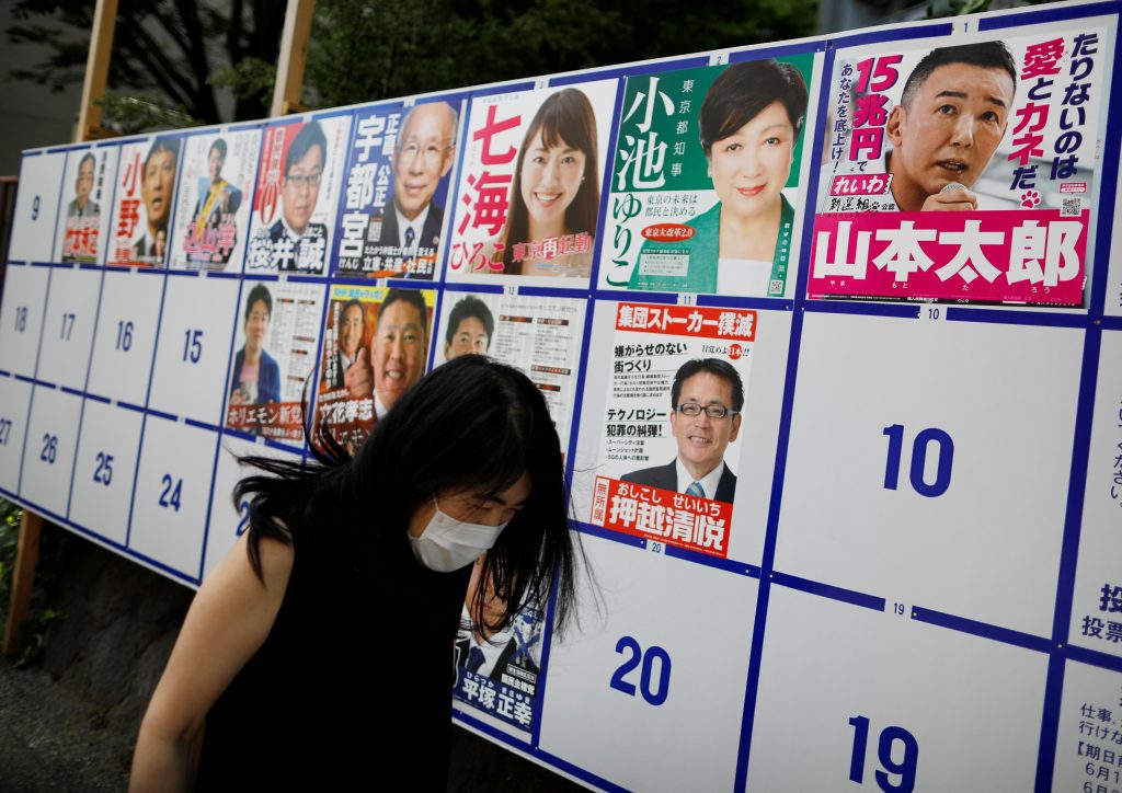 コロナウィルス感染症（COVID-19）の拡散が続く中、もうすぐ行われる東京都知事選のための、現都知事小池百合子を含む候補者のポスターの前を歩いて通り過ぎるマスクを着けた通行人。2020年7月2日、東京。（ロイター）