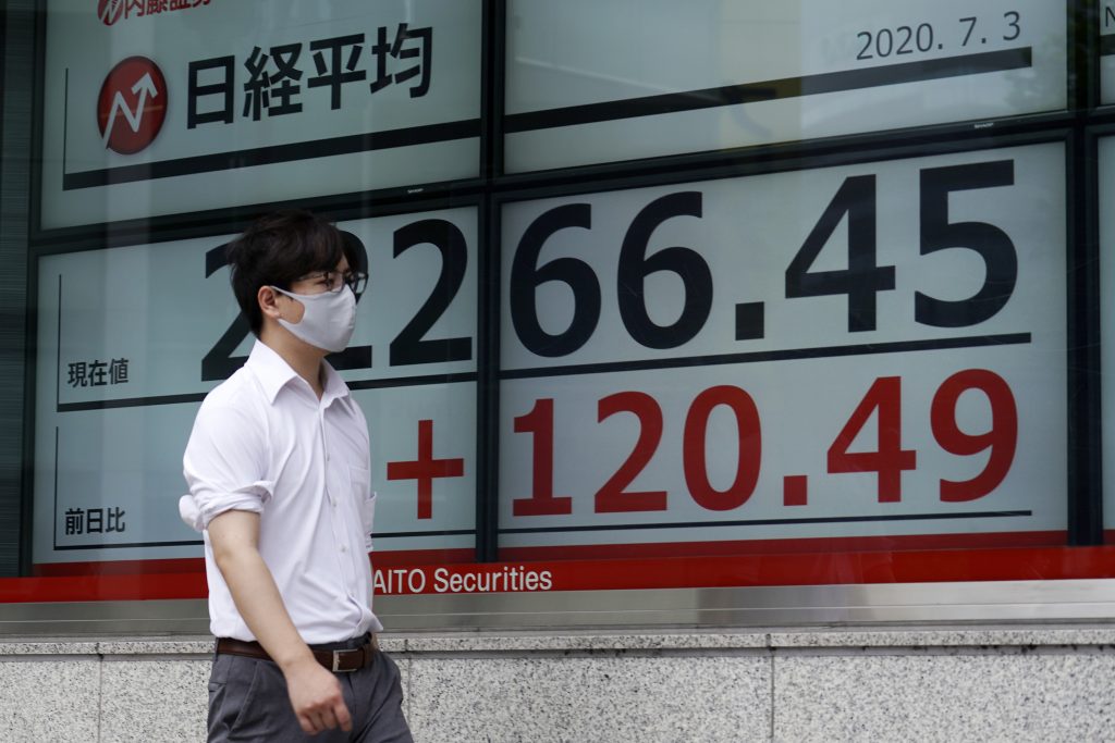 日経平均株価を表示する東京の証券会社の電光掲示板のそばを歩いて通り過ぎる男性。(2020年7月3日、資料写真=AP)