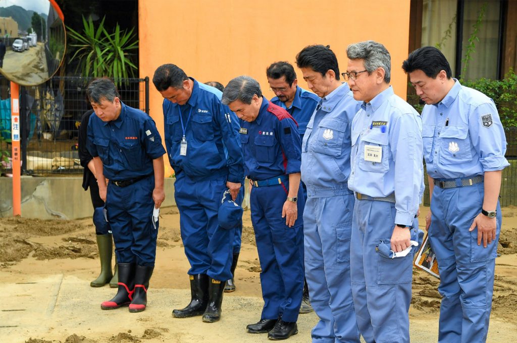 2020年7月13日、先週の豪雨と浸水により壊滅的な被害を受けた後14人が死亡した老人ホーム千住園の外で静かな祈りを捧げる日本の安倍晋三首相（右から3人目）。（資料画像・AFP）