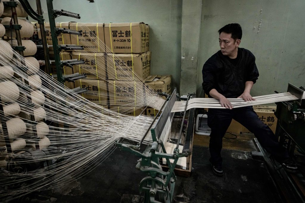 大阪府柏原市の工場で、柔道着を製造する年代ものの織機をチェックする、日本の武道用具メーカー九櫻のスタッフ。2020年2月25日撮影。（AFP）