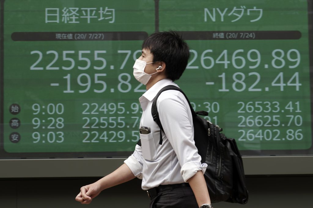 2020年7月27日、日本の日経225とニューヨークのダウ平均株価を表示する東京都内の証券会社の電子株価ボードの前を歩く男性。（ファイル　写真）