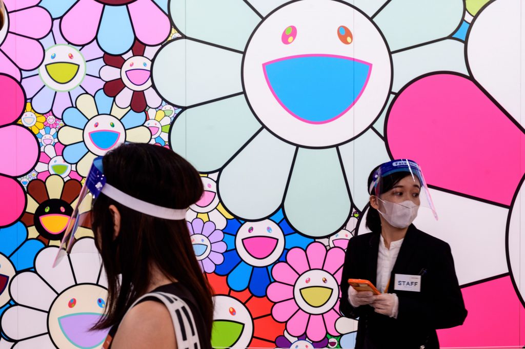 東京の森美術館で開催された「STARS展：現代美術のスターたち― 日本から世界へ」のプレス向け内覧会で、村上隆の『ポップアップフラワー』の横でフェイスシールドを付けて立つ美術館スタッフ。2020年7月30日に撮影。（AFP）