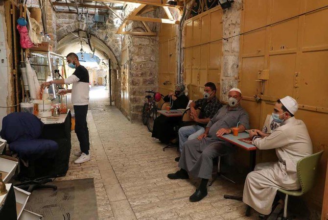 新型コロナウイルス感染症（COVID-19）のパンデミック危機の中、ヨルダン川西岸地区の町・ヘブロンの旧市街で保護マスクをつけて座り込むパレスチナ人＝2020年7月10日。(AFP)