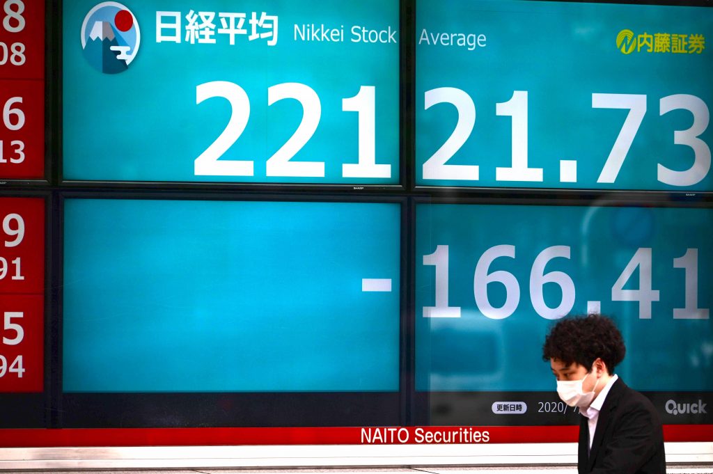 2020年7月1日、東京で、フェイスマスクをつけた人物が日経225指数の数値を示す株価電光掲示板の正面を歩いている（画像ファイル/AFP通信）