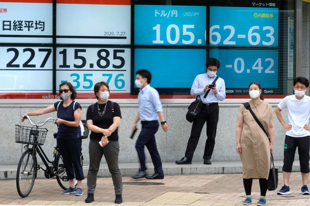 東京の東京証券取引所(左)で株価指数と並んで米ドルの対日本円為替レートを表示する相場ボードの前に立つ歩行者たち。2020年7月27日。(資料写真/AFP)